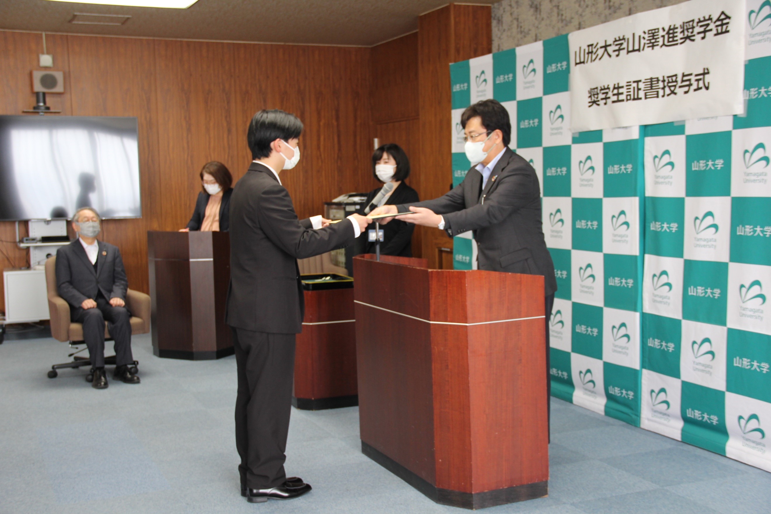 奨学生証書授与（右：山澤代表理事、左：理学部・齋藤さん、左奥：玉手学長）の画像