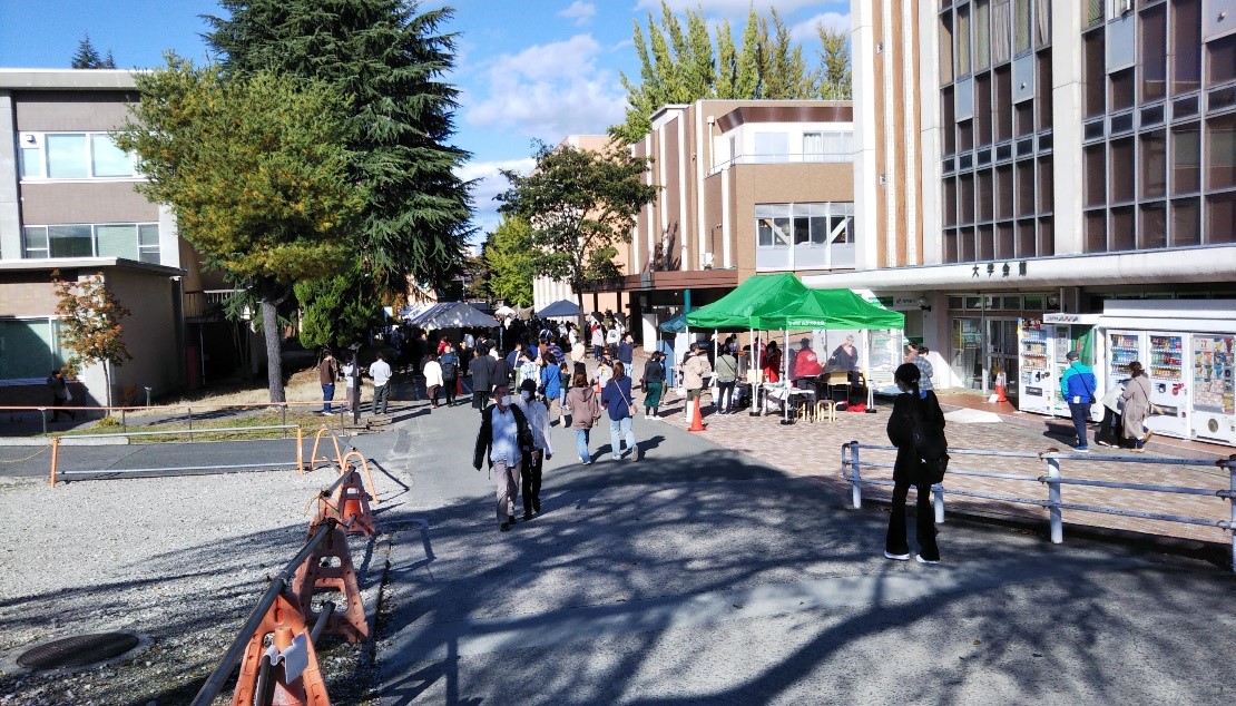 写真2．教養坂から第1体育館への道路沿いに建てられたテントと参加者たち。の画像