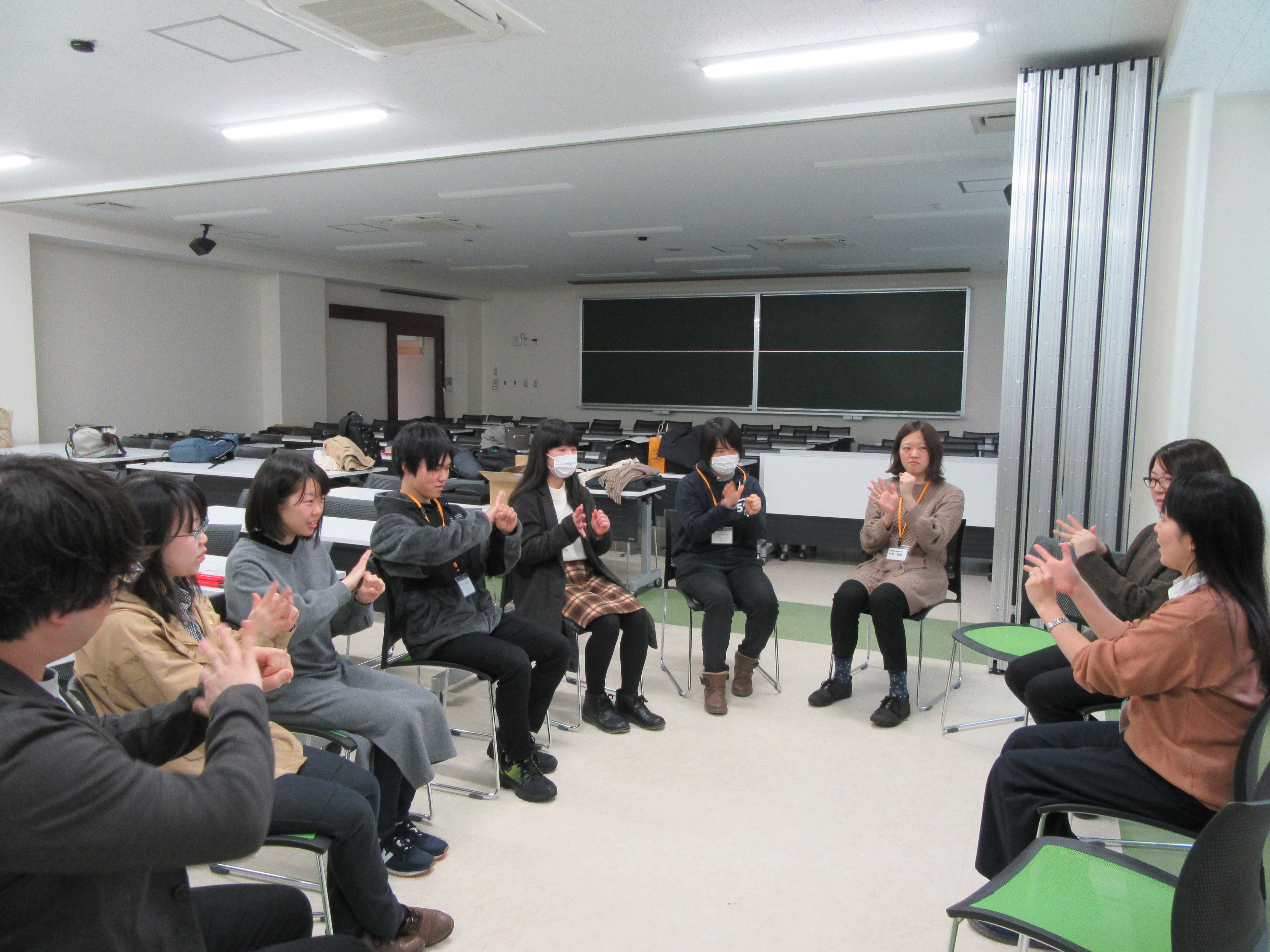 講師と受講生数名が輪になって座り、手話を学んでいる