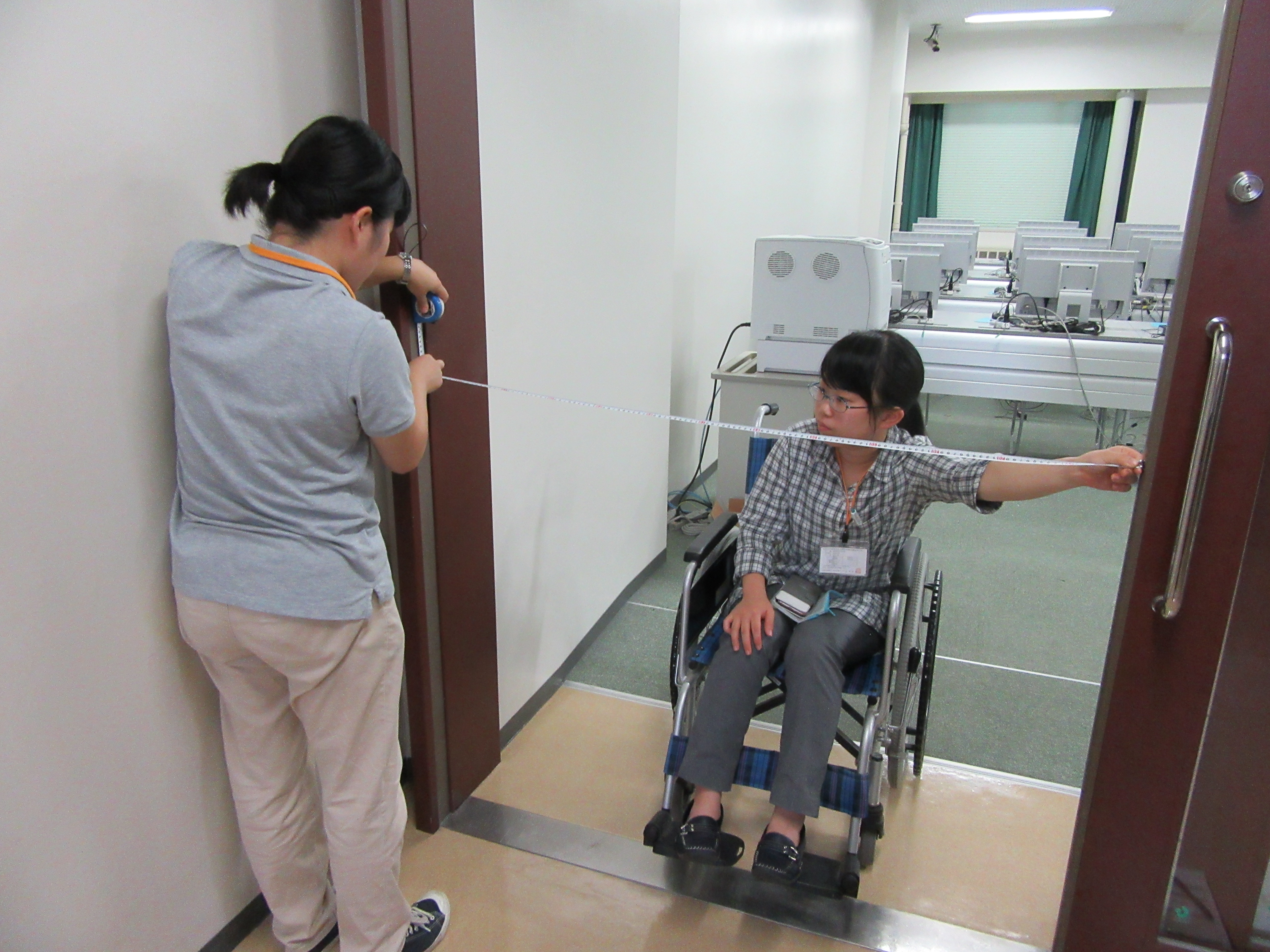 支援学生が車いすに乗り、もう1人とドアの長さを測っている