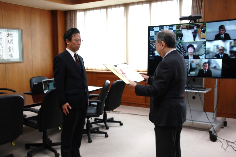 受賞者を代表して学長より表彰状と副賞を授与される本山功教授（左）の画像