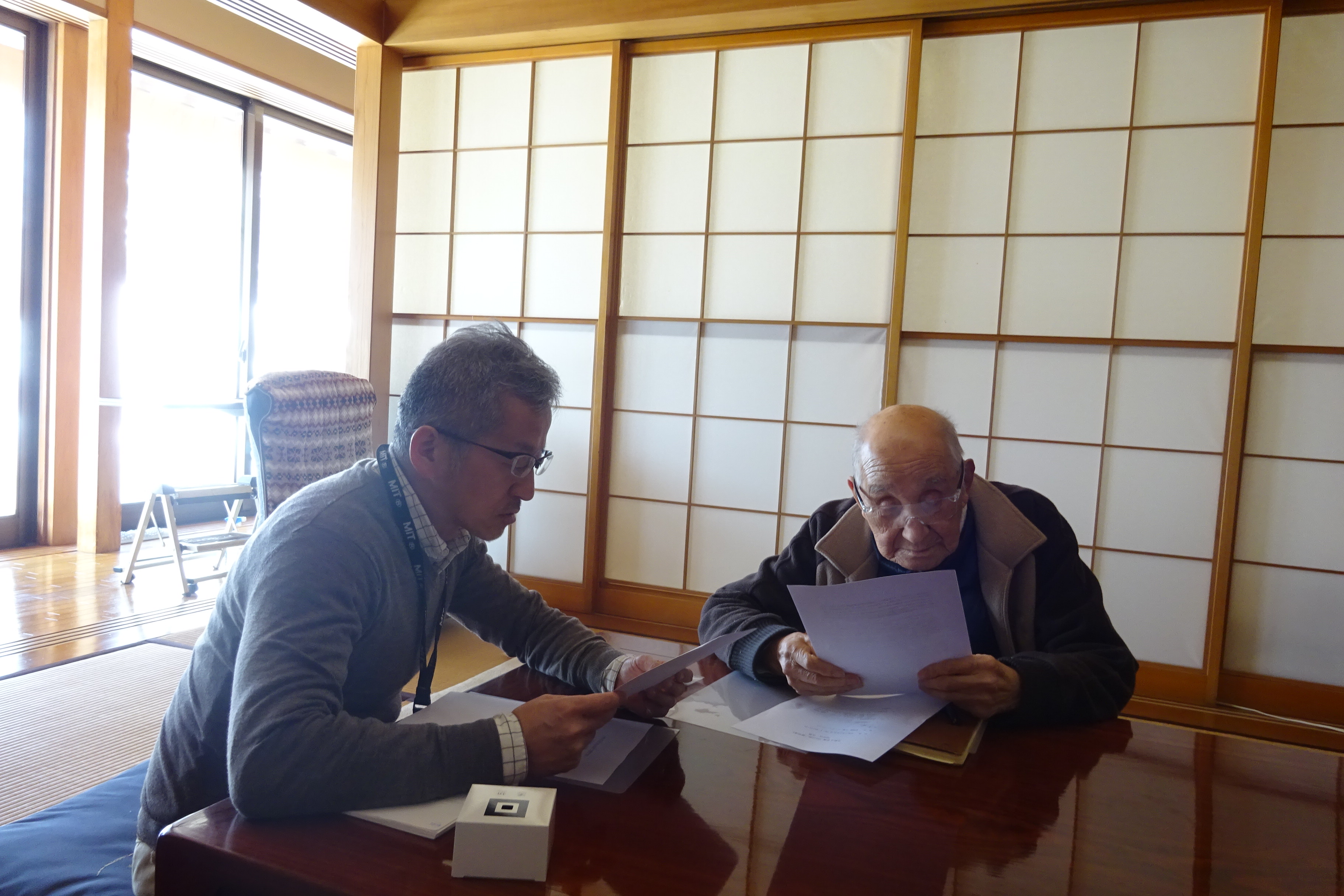 山口祥二様（右）に学生の御礼メッセージを報告する樋口室長の画像