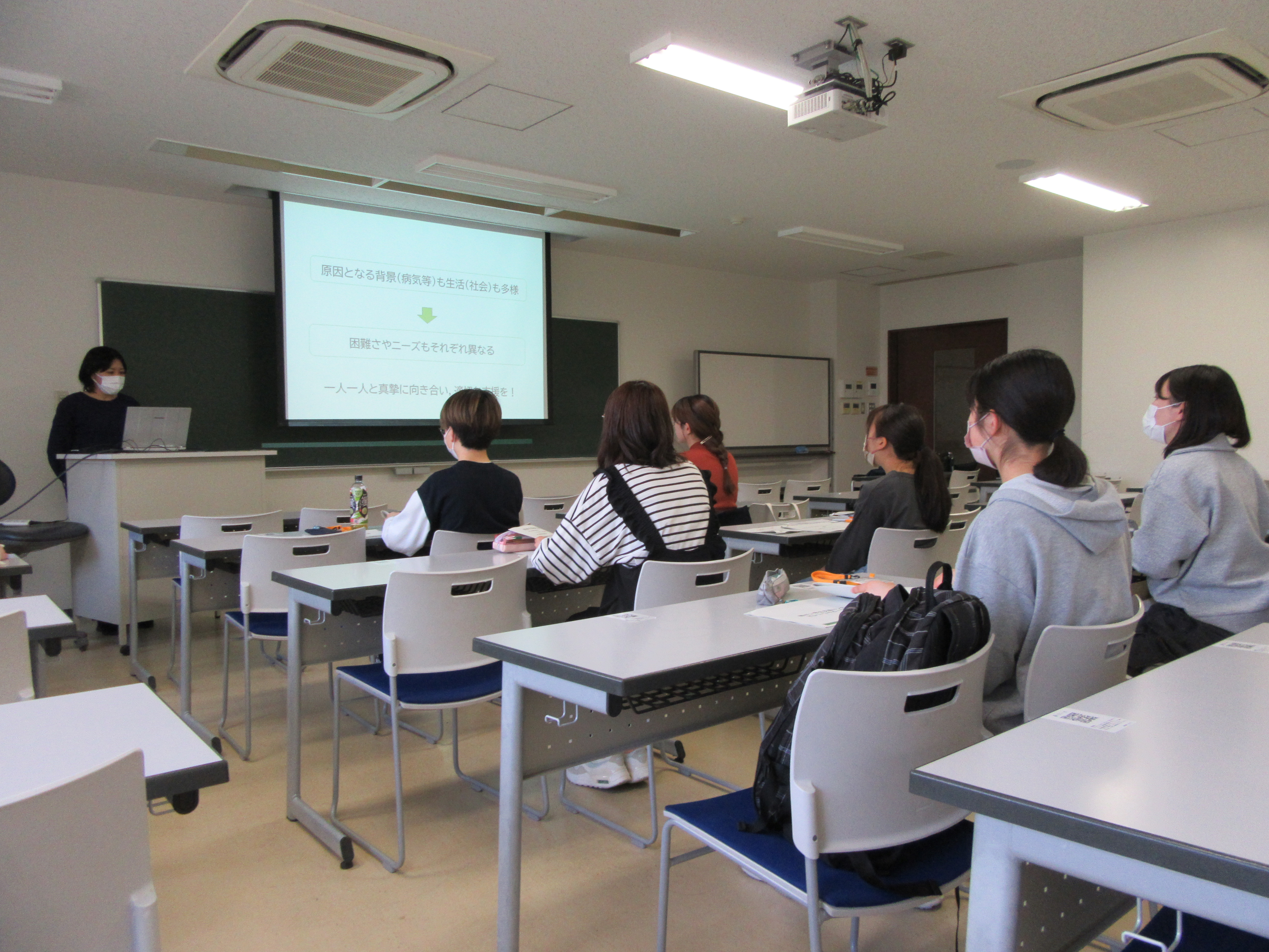 講師の先生が前に立ち、参加者の皆さんが椅子に座っている。パワーポイントを用いた講義を聞いている。